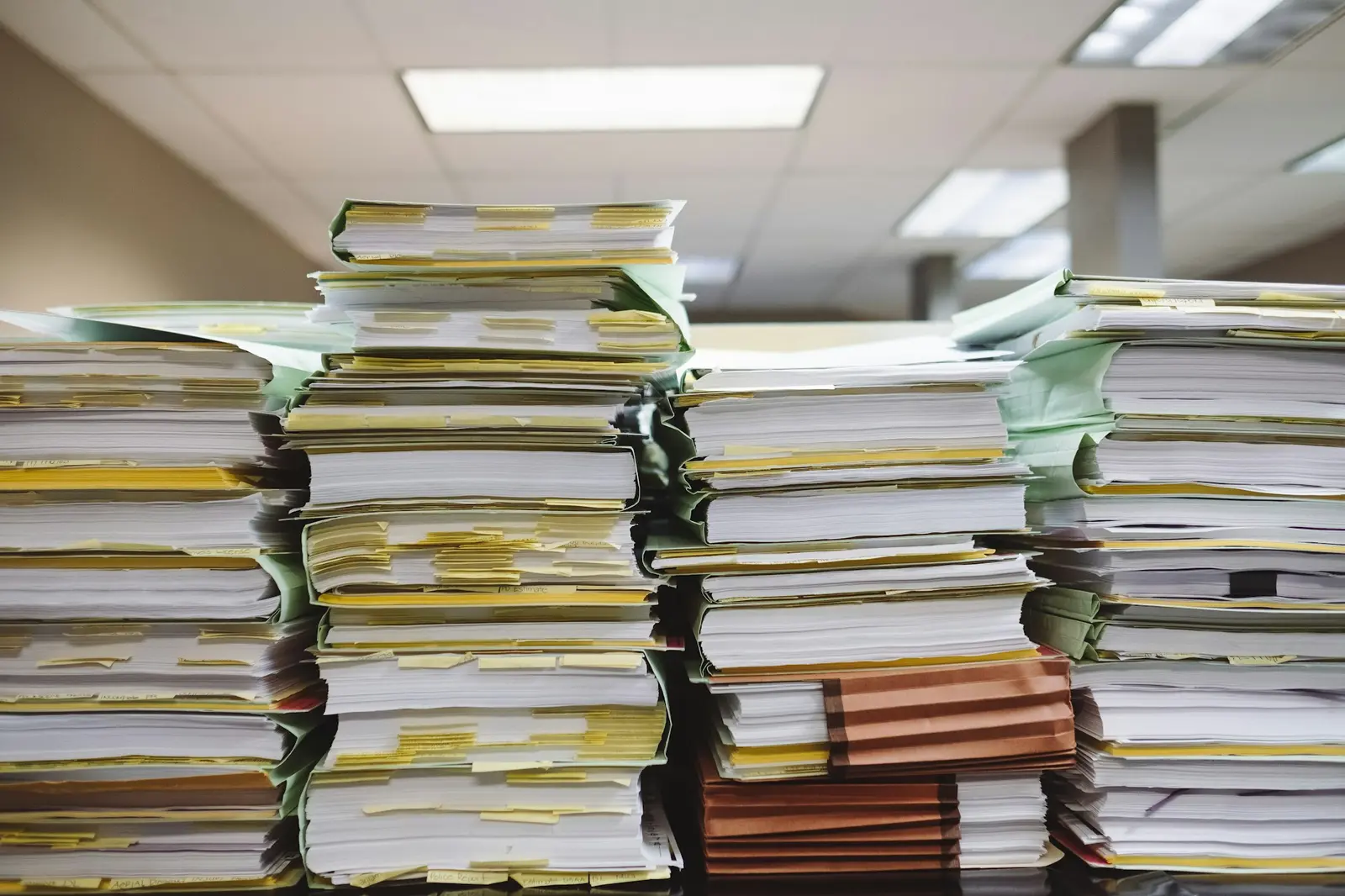 Pilhas altas de processos em papel sobre mesas de escritório