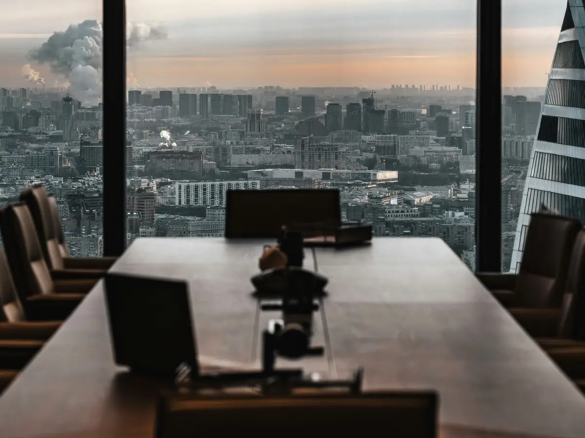 Sala de reunião de escritório no alto de um edifício, com mesa longa e a cidade ao fundo, ao entardecer