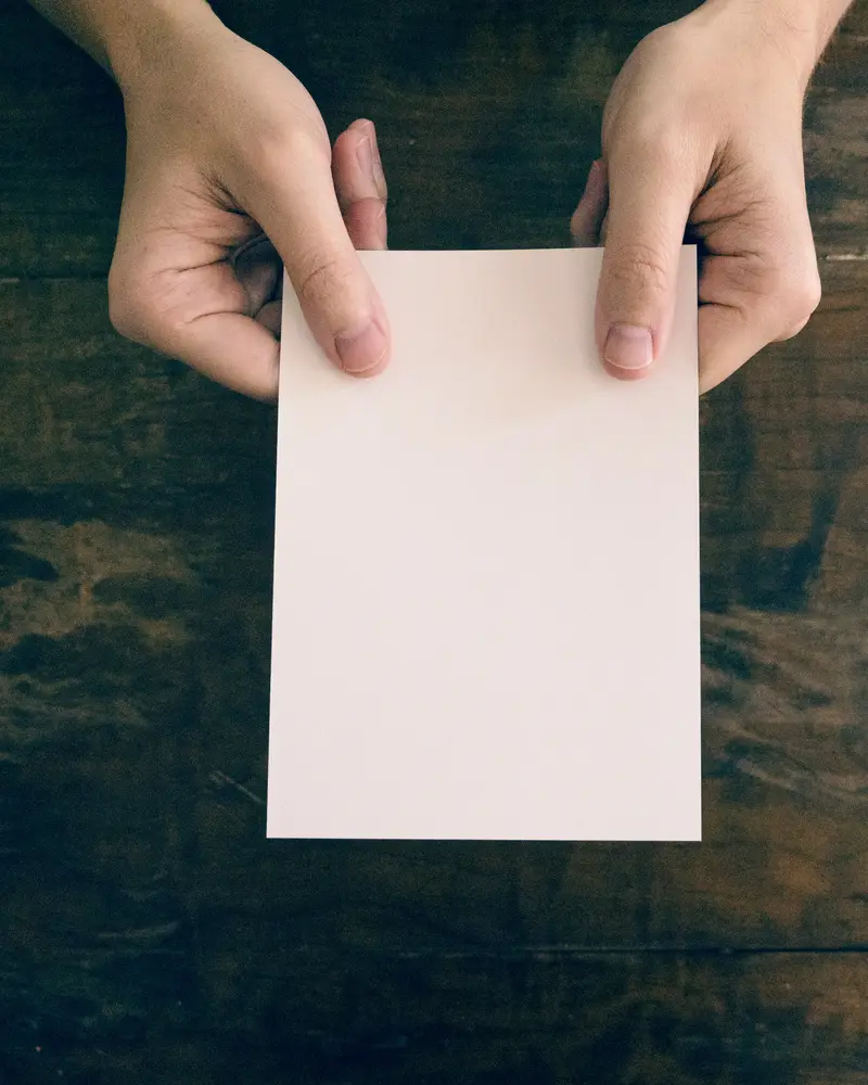 Mãos segurando uma folha de papel sobre uma mesa de madeira escura