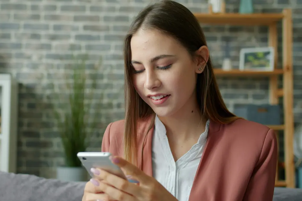 Mulher consulta o celular com atenção, sentada no sofá de casa